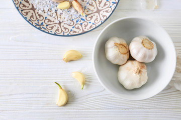 Bowl with fresh garlic on white wooden background