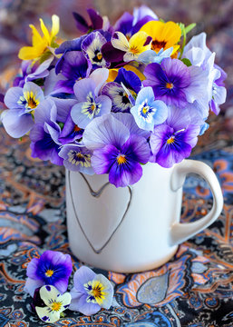Photo of a beautiful purple pansy flowers close-up in a mug on a colorful background. Beautiful and delicate flowers.