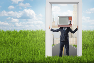 Businessman with old TV set instead of head standing in a doorway from city to the country