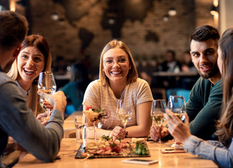 Group of young friends having fun in restaurant, talking and laughing while dining at table.