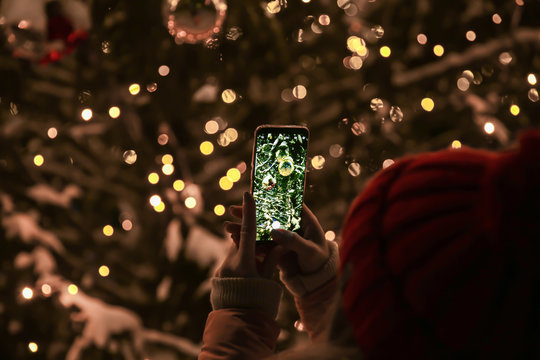 Woman taking picture of beautifully decorated Christmas tree outdoors