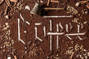 Calligraphic inscription gothic letters coffee over ground black coffee scattered on white marble with roasted and unroasted beans, vintage pot. Coffee drinking concept background. Top view