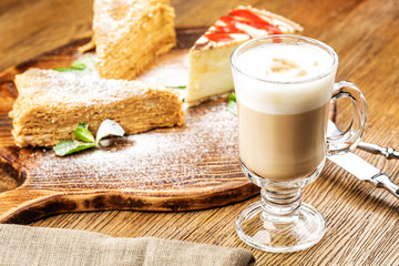 A freshly prepared Cup of frothy lette coffee is served with a piece of cake. On a wooden table.