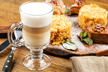 A freshly prepared Cup of frothy lette coffee is served with a piece of cake. On a wooden table.
