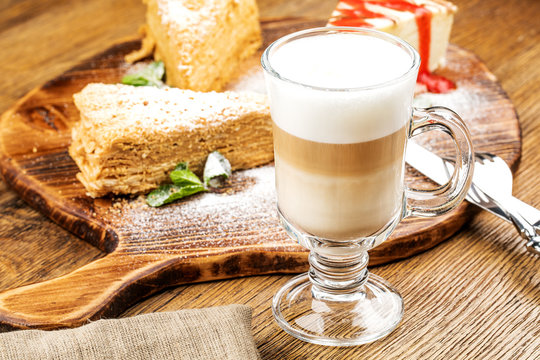 A freshly prepared Cup of frothy lette coffee is served with a piece of cake. On a wooden table.
