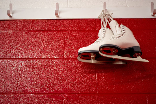 Bottom view of figure skates hanging over red wall in locker room with copy 
