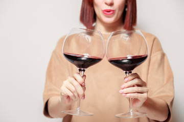 Redhaired girl sommelier on white background and hold with two glasses of red wine. Concept alcoholism, alcohol addiction, bad habit, collection rare wine, blind degustation