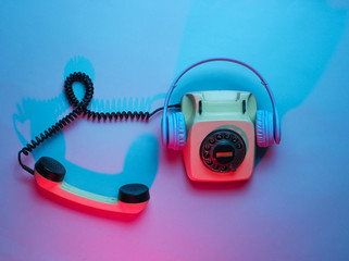 Vintage rotary phone with headphones. Retro wave, red blue neon light, ultraviolet. Top view,...