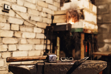 closeup of a blacksmith anvil with a hammer, tongs and firesteel.