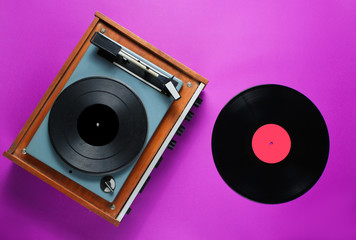 Retro 70s vinyl record player with a vinyl record on a purple background. Top view, minimalism