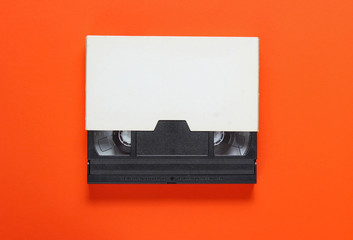 The videotape in a paper case on orange background. Pop culture attributes, minimalism. Top view