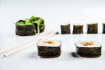 Two chopsticks, sushi and rolls on white background