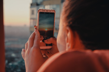 Close-up woman taking picture of sunset with her smartphone from skyscrapper