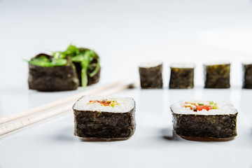 Two chopsticks, sushi and rolls on white background