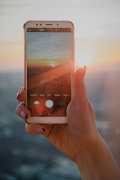 Woman hand taking picture of sunset landscape with smartphone from roof top