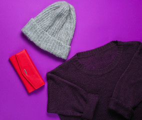Women's fashion items on a purple background. Sweater, warm hat, red purse. Top view