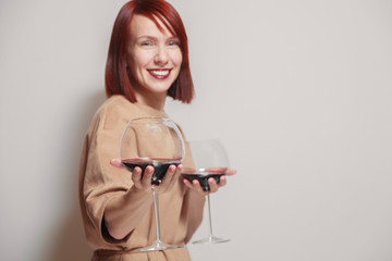 Young cheerful redhaired girl sommelier on white background smile and hold with two glasses of red...