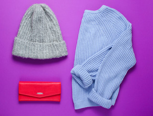 Women's fashion items on a purple background. Sweater, warm hat, red purse. Top view