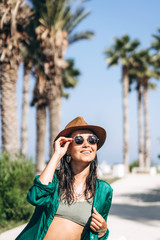 Cute pan asian girl in hat and sunglasses in green pareo walking on the seaside.