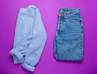 Women's jeans and sweater on a purple background. Top view. Minimalism