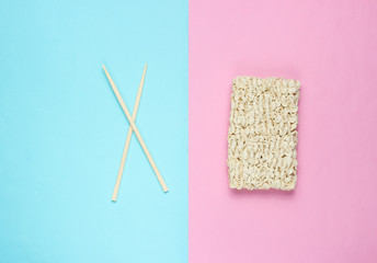 Raw instant noodles and chinese chopsticks on pastel background, minimalism