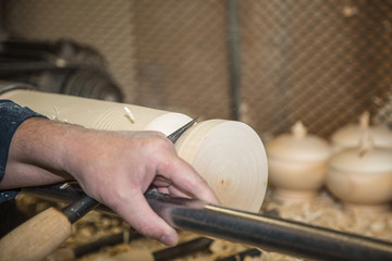 Men's hands holding a chisel near the lathe on wood