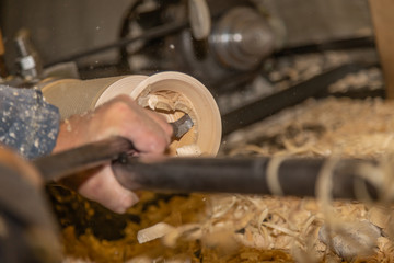 Men's hands holding a chisel near the lathe on wood