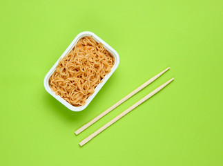 Instant noodles and chinese chopsticks on green background, minimalism. Top view