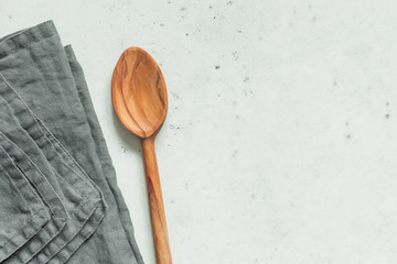 Wooden spoon and grey linen napkin on a white kitchen table. Top view, copy space.