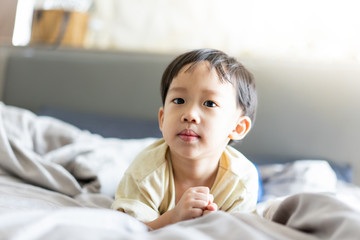 A kid is playing in the morning while watching TV in the bed in the bedroom.