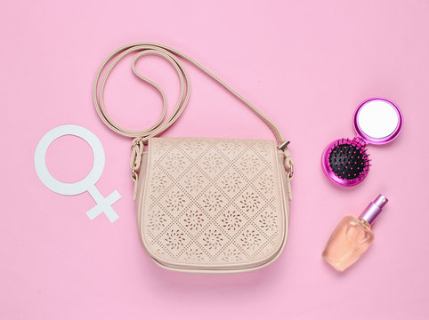 Women's accessories. Leather fashion bag, perfume bottle, mirror comb, gender feminism symbol on pink background. Top view. Minimalism
