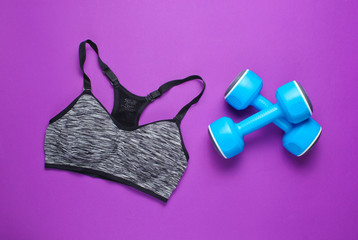 Fitness concept. Sports bra, dumbbells on a purple background. Top view, minimalism