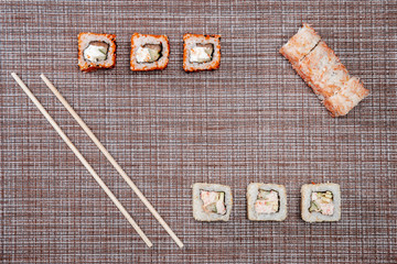 Two chopsticks, sushi and rolls on braided brown background