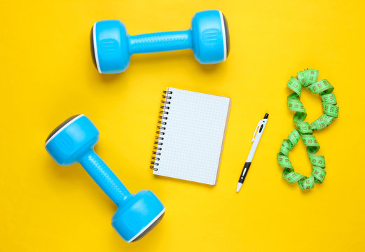 Fitness concept, workout plan. Plastic blue dumbbells, notepad, ruler on a yellow background. The idea of ​​losing weight. Top view. Flat lay