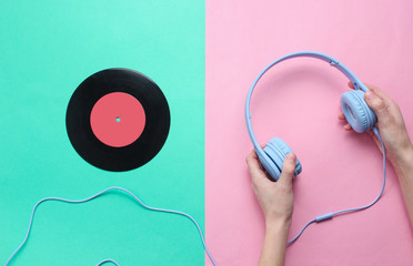 Women's hands hold headphones and vinyl record on pastel background. Pop culture, retro style, 80s. Minimalism. Top view. Flat lay