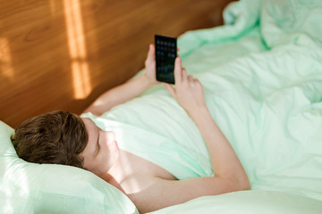 A young man in bed with a smartphone in hands