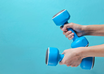Female hands hold plastic dumbbells on a blue background. Copy space