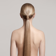 woman with a hair tail. Back view. Gray background. light brown hair color toning