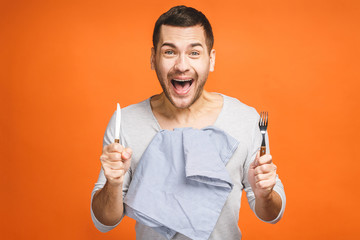 Young hungry crazy man holding a fork and a knife. Isolated on orange background.