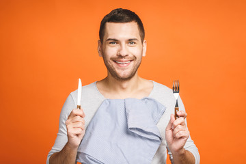 Young happy smiling crazy man holding a fork and a knife. Isolated on orange background.