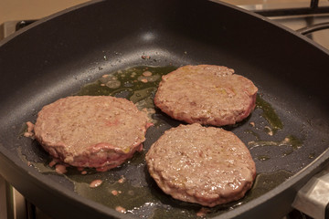 Greasy hamburger patty frying in a pan