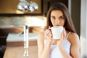Beautiful young woman holding mug in her hand while relaxing at home