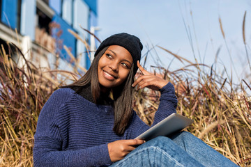 Portrait of a beautiful young smiling african woman using tablet pc computer sitting in the city in a sunny day