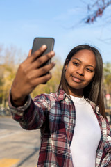 Portrait of a young african american woman standing outdoors while taking a selfie in sunny day