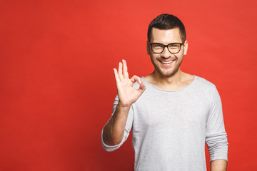 Happy handsome man showing ok sign. Isolated over red background.
