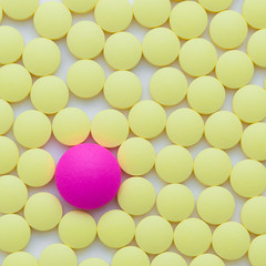 Small yellow and one pink pills on a white background close-up.