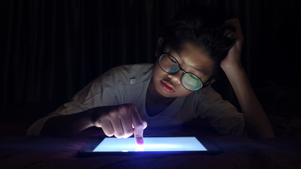 Asian boy pressing digital tablet at night with serious face.