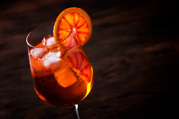 Aperol spritz cocktail in big wine glass with bloody oranges, summer Italian fresh alcohol cold drink. Wooden bar counter background, selective focus