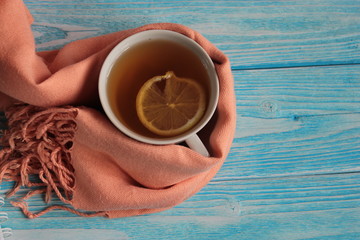 Mug of tea with lemon and scarf on a wooden table.