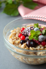 Healthy breakfast in a bowl with oatmeals, frozen berries, fresh strawberries, mint. Oat porridge with fruits.